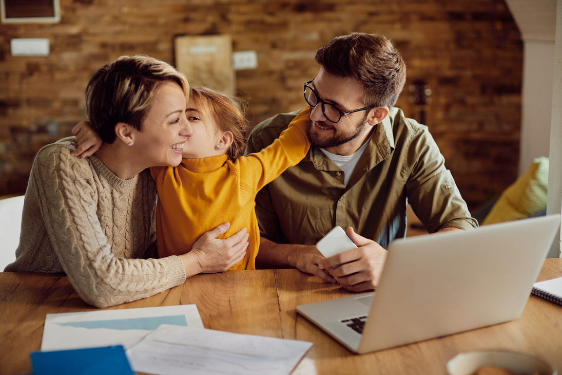 Happy daughter embracing and kissing her working parents at home.